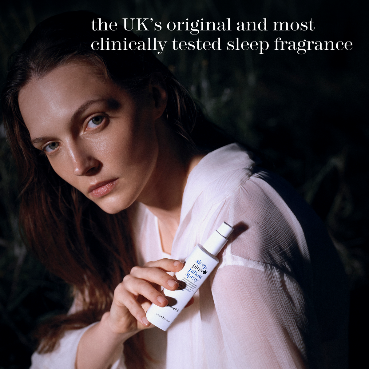 A woman in a white top holds a bottle of this works sleep plus pillow spray against a dark, moody background. White text at the top reads, 'the UK's original and most clinically tested sleep fragrance.